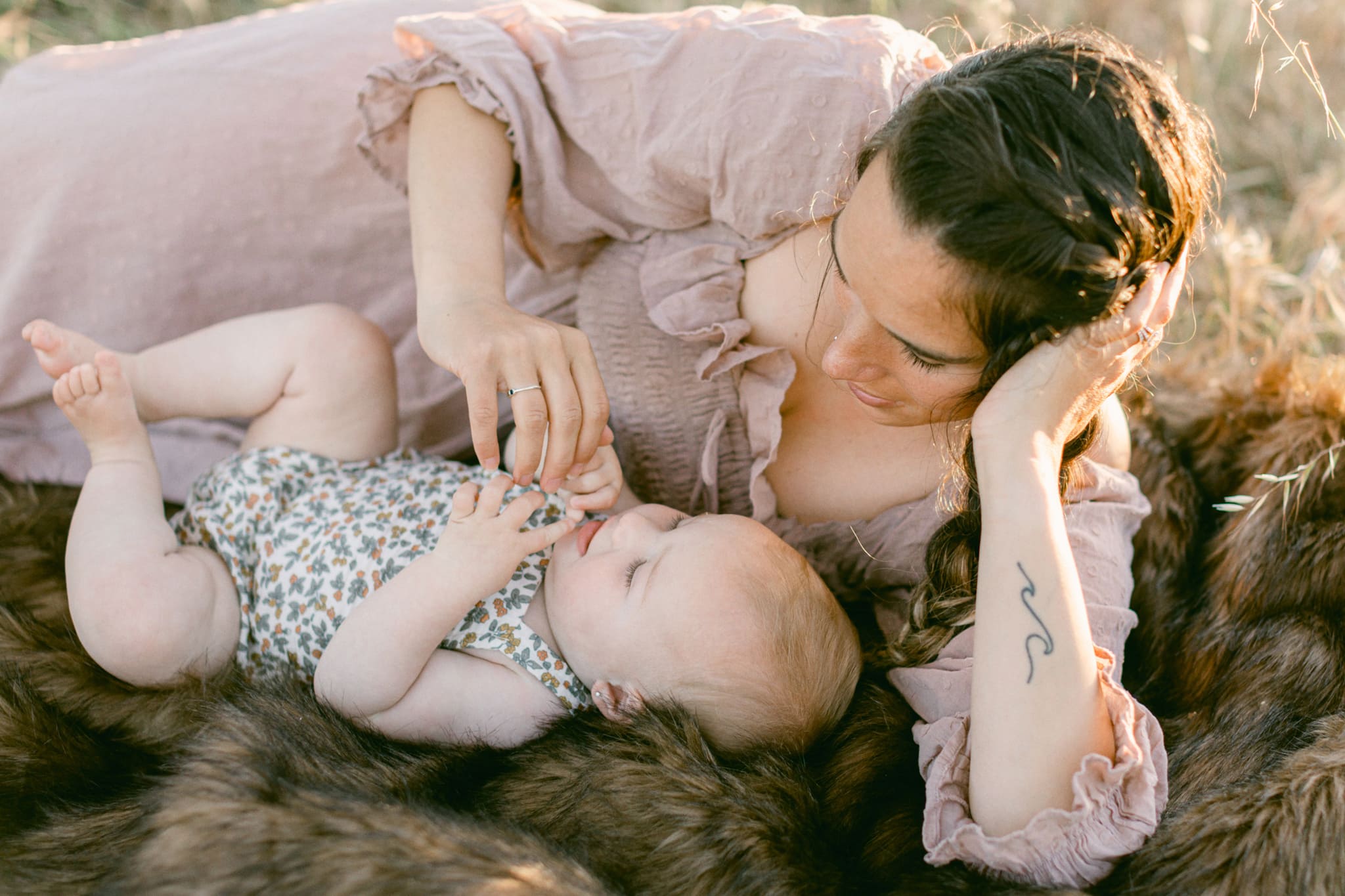 Mother and daughter laying on blanket while mother plays with her hands during their motherhood photography session.