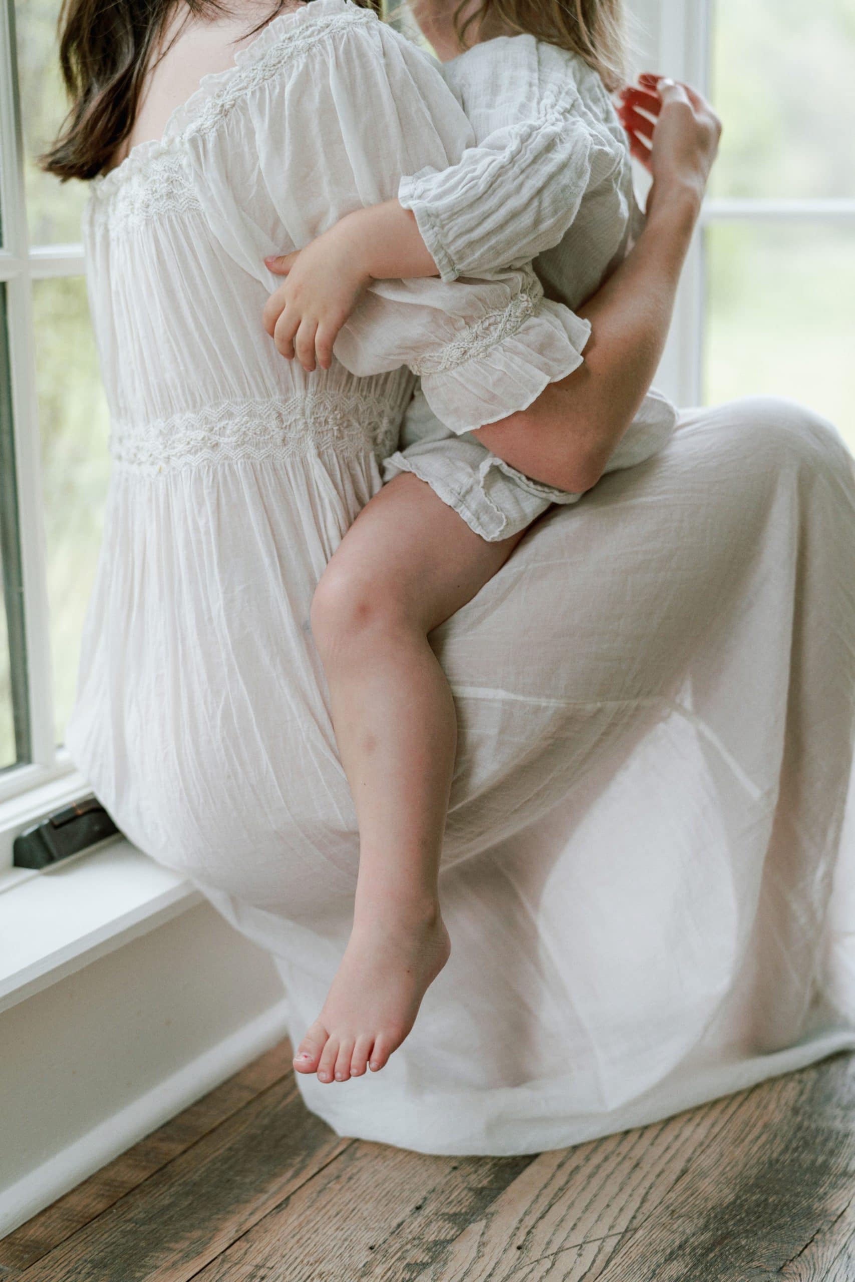 Indoor family session, mother is holding daughter tightly while sitting on the ledge by the stairs.