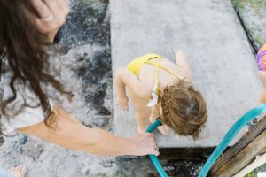 Documentary family photographer, little girl drinking water from hose.