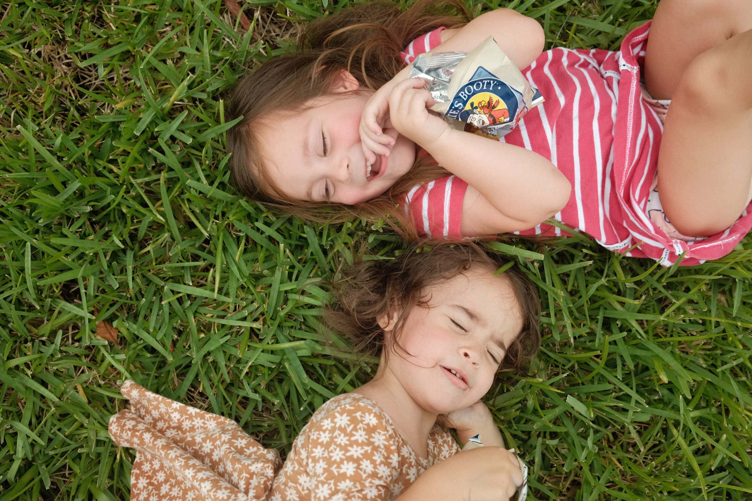Two girls being silly on the grass while they are photographed during their family documentary session.