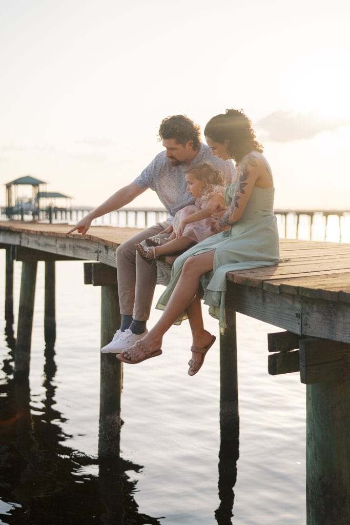 Family enjoying a sunset by the water on a wooden dock.