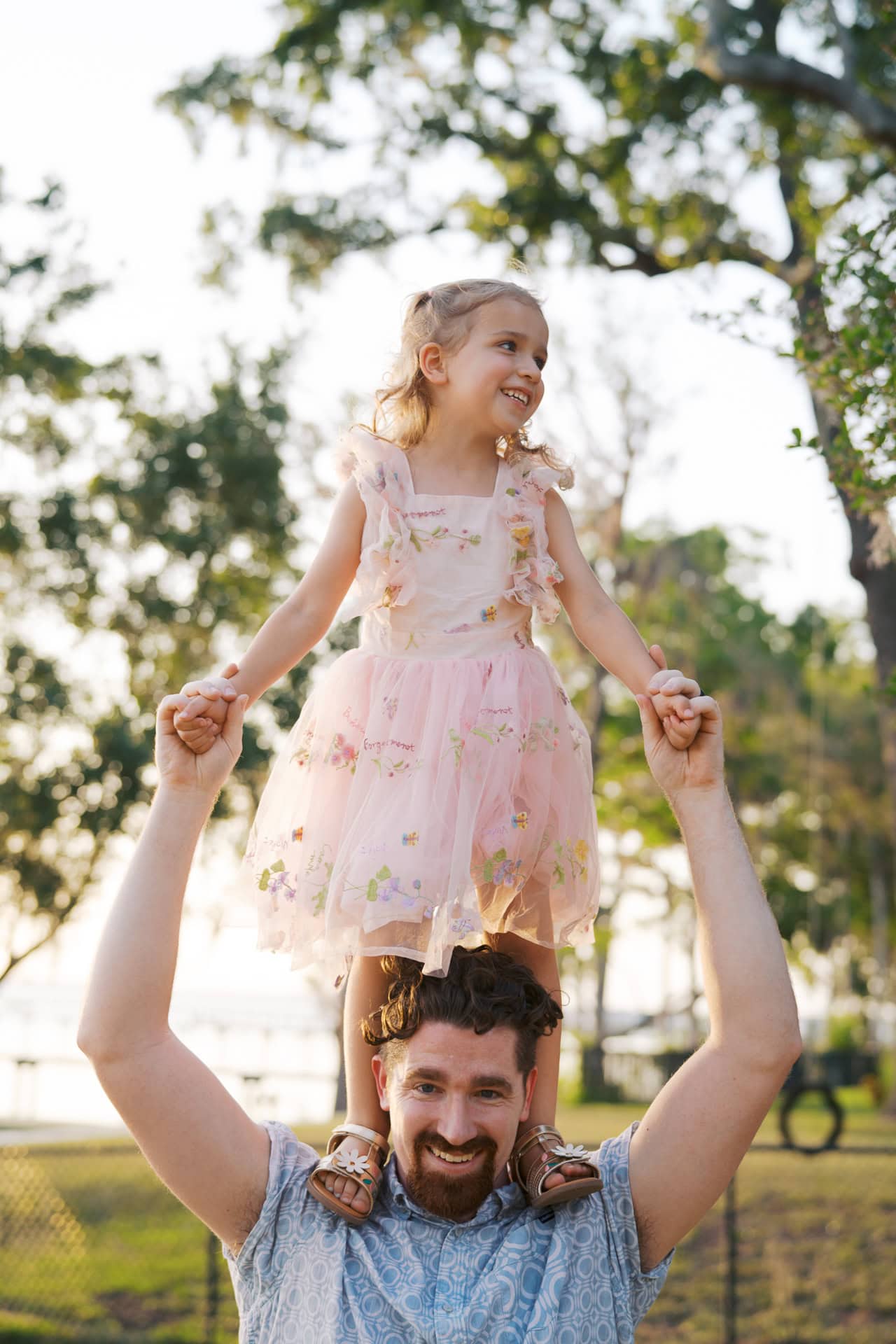 Happy father lifting young girl in a park during their outdoor family photo session.
